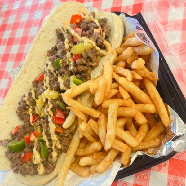 Classic Gourmet Deli's cheesesteak with peppers and sauce, served with golden french fries on a red checkered tablecloth.