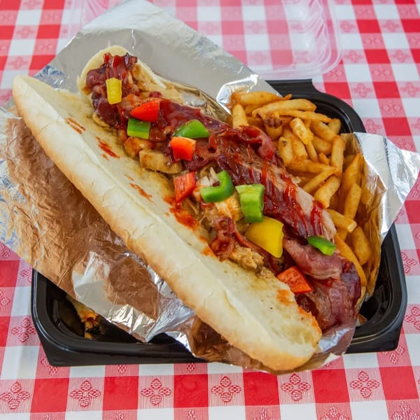 Classic Gourmet Deli's loaded sub sandwich with peppers, sauce, and fries on a red checkered tablecloth.