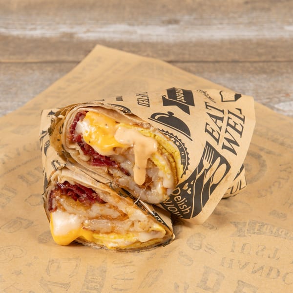 A breakfast burrito, cut in half, revealing eggs, cheese, bacon, and sauce, wrapped in branded paper.