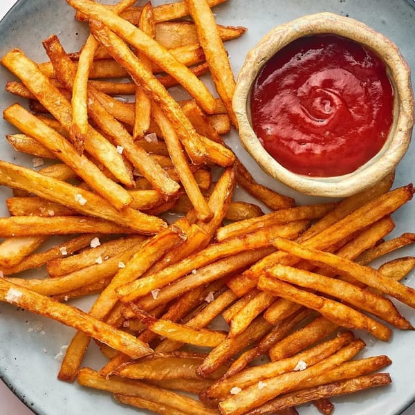 Golden-brown french fries with sea salt on a plate, next to a small bowl of ketchup.
