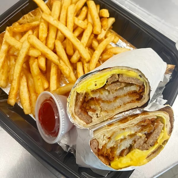 Classic Gourmet Deli's breakfast burrito, cut in half, with fries and ketchup in a black to-go container.
